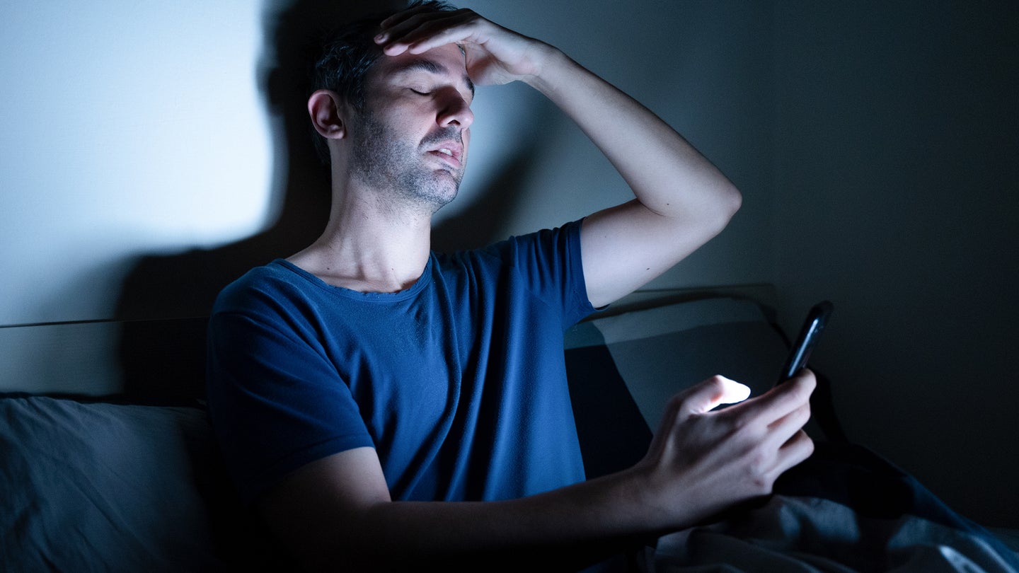 Man doomscrolling in bed alone at night