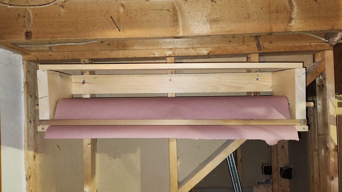 A wall-mounted paper roll holder attached to a wood-framed wall near a low ceiling in a workshop.