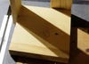 A piece of wood for a DIY paper roll holder, with a mark on it for where a hole will need to be drilled to hold the dowel that holds the roll.