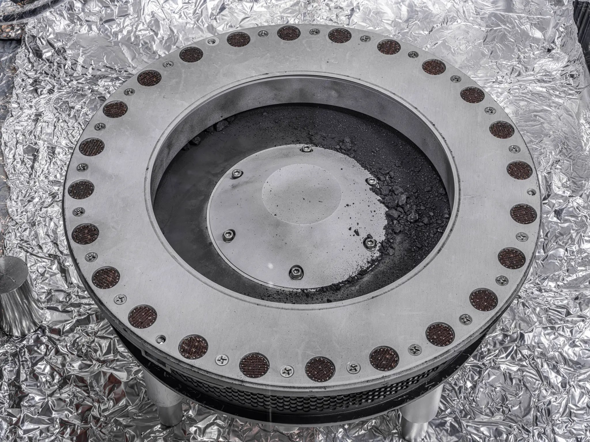 A view of the outside of the OSIRIS-REx sample collector. Dark sample material from asteroid Bennu can be seen on the middle right. Scientists have found evidence of both carbon and water in initial analysis of this material. The bulk of the sample is located inside. 
