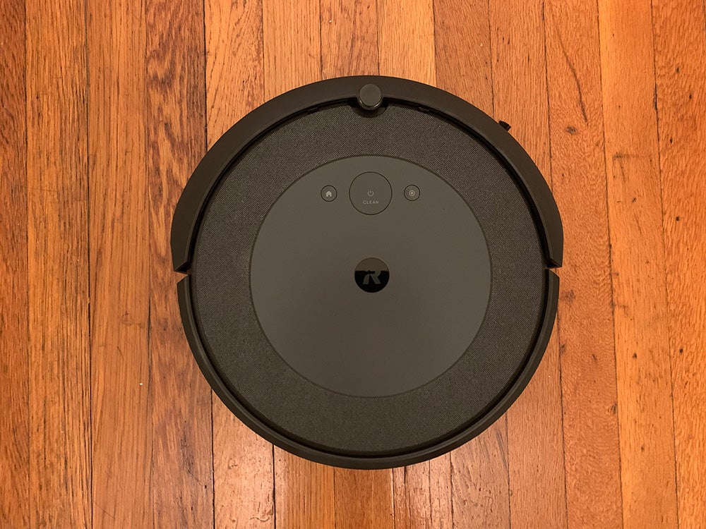 A round black iRobot Roomba i4 against a wooden floor.