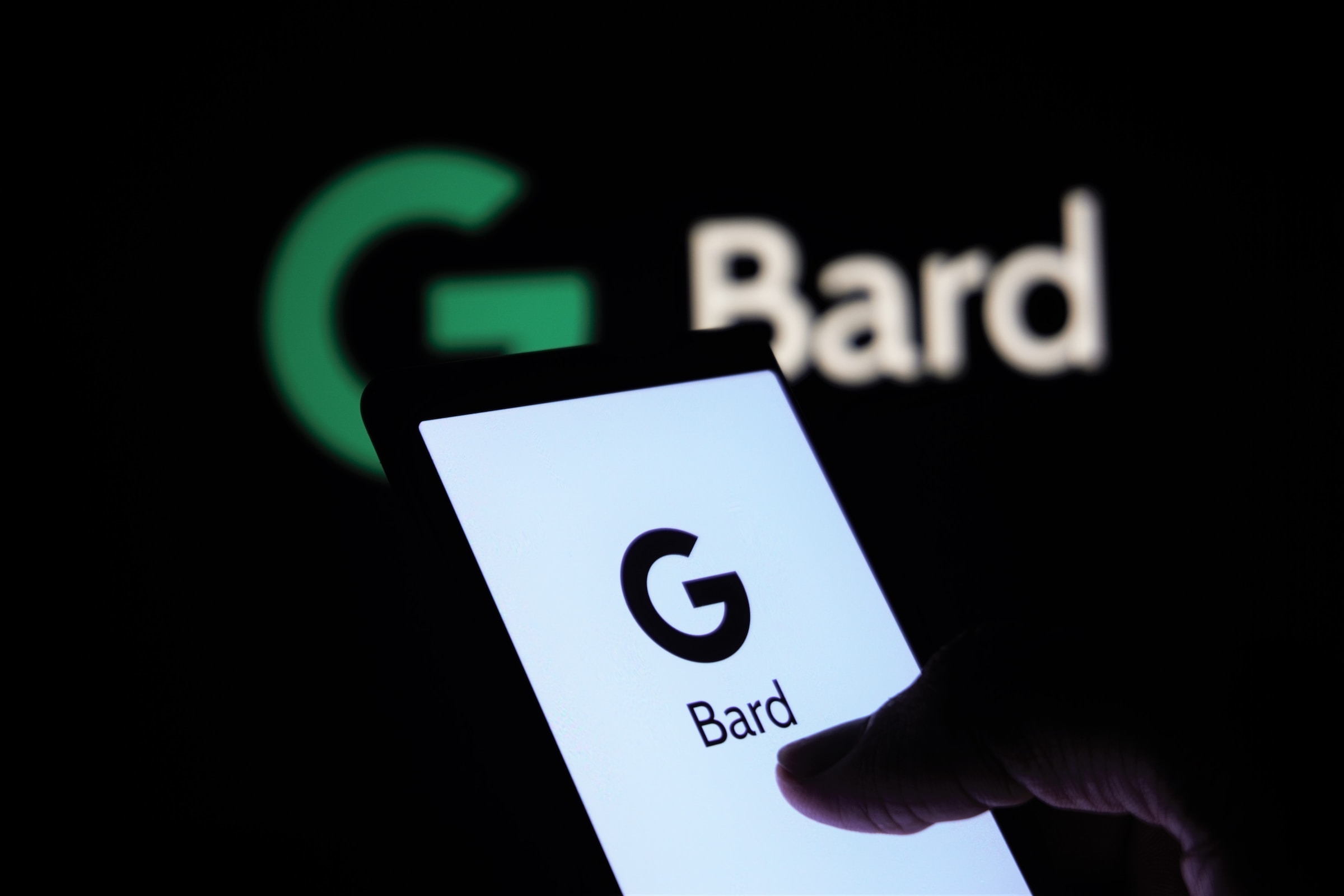 A person holding a phone in a very dark room, with Google Bard on the screen, and the Google Bard logo illuminated in the background.