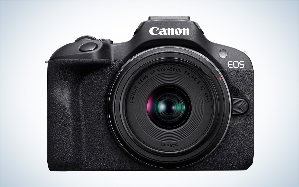 The Canon EOS R100 mirrorless camera is placed against a white background with a gray gradient.