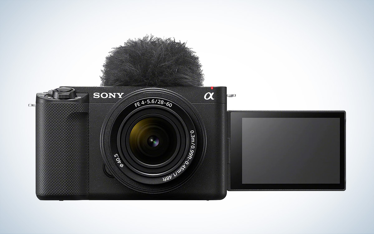 The Sony ZV-E1 mirrorless vlogging camera with a mic wind muff attached is placed against a white background with a gray gradient.