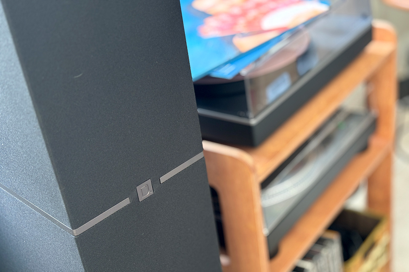Closeup on black Definitive Technology DM70 floorstanding speaker with a turntable in the background