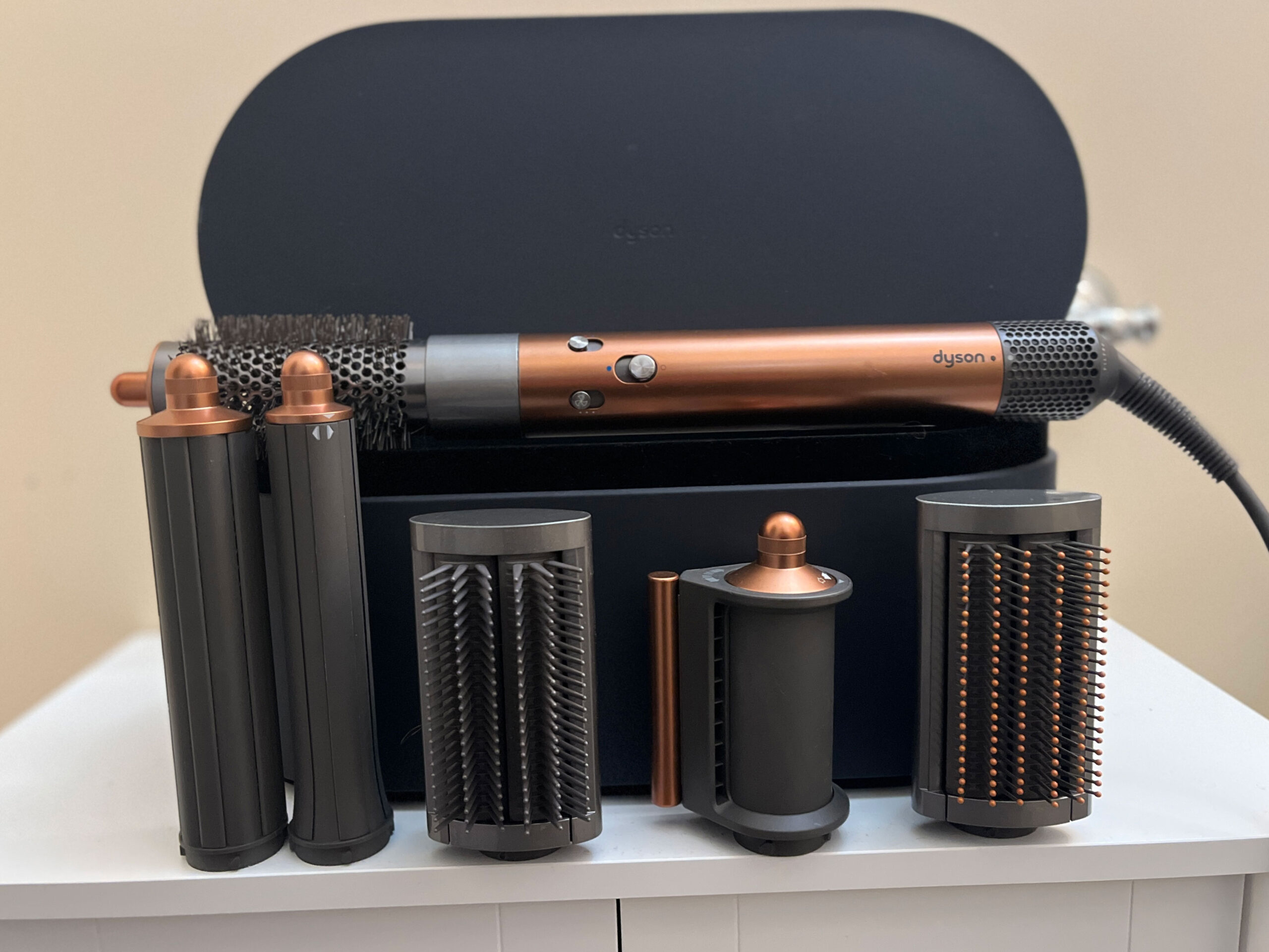 A copper and silver Dyson Airwrap displayed on a white shelf against a yellow wall