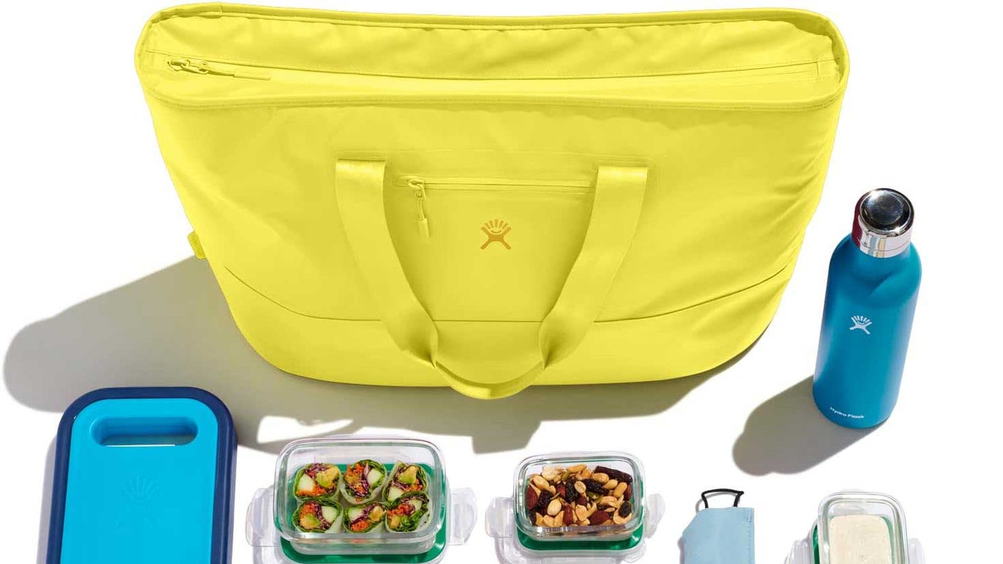 A Hydroflask bag with a hydroflask water bottle and a picnic laid out on a plain background