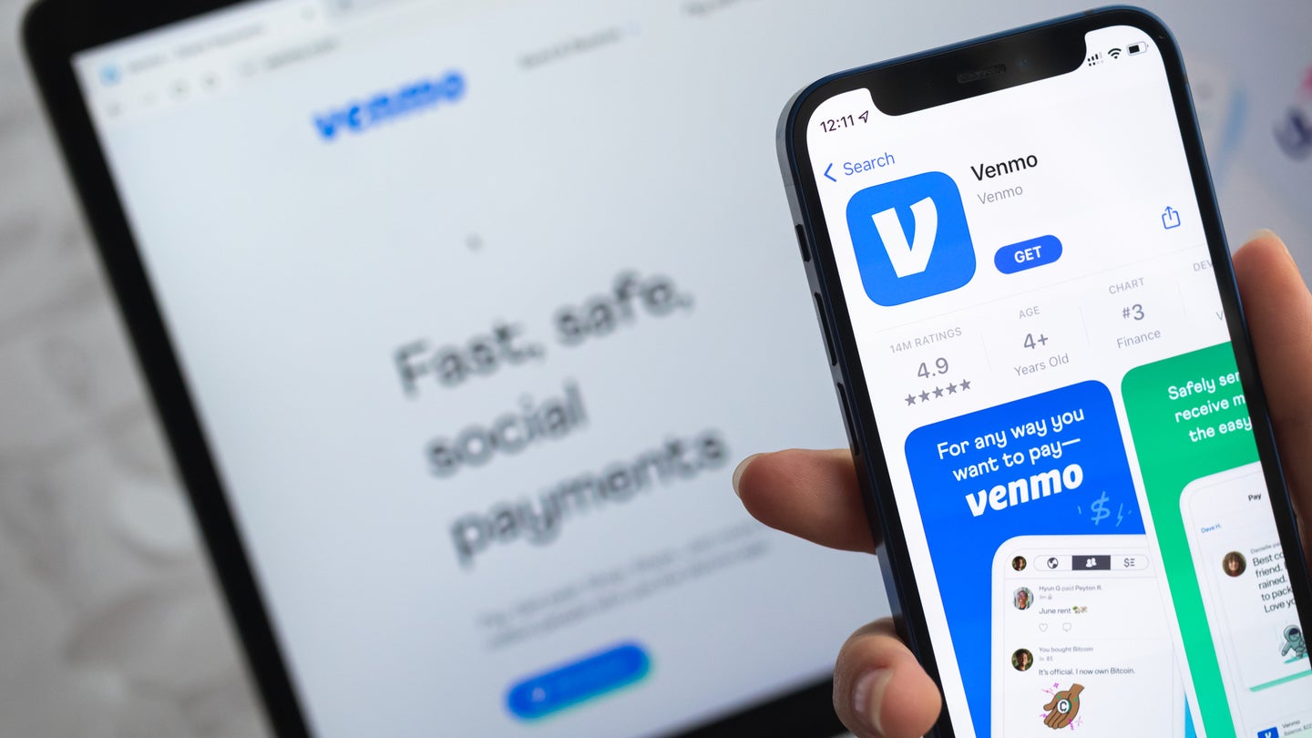 Hand holding smartphone with Venmo app download in front of Venmo website on computer