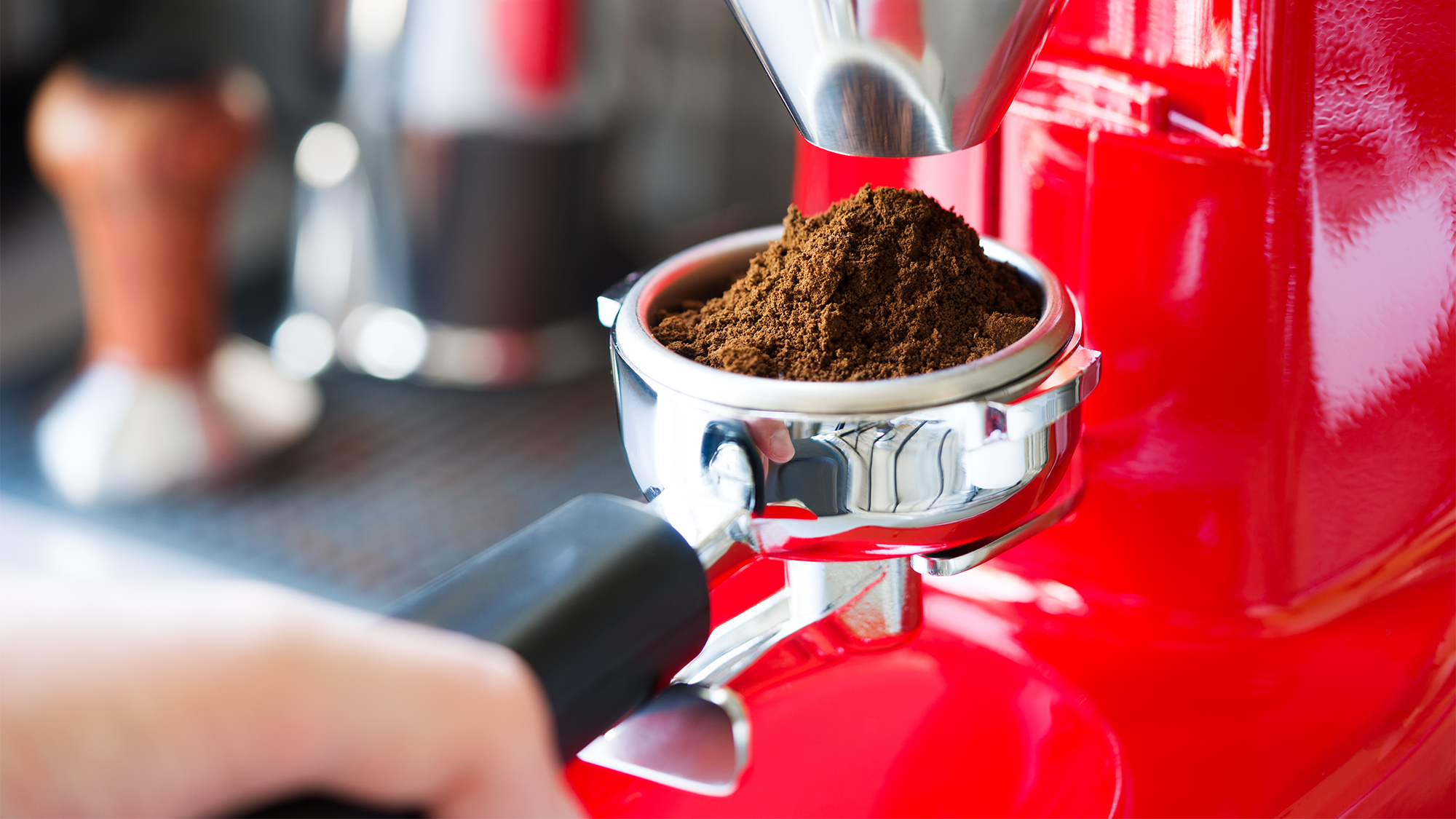 Finely ground bits of coffee come out of a red coffee grinder.