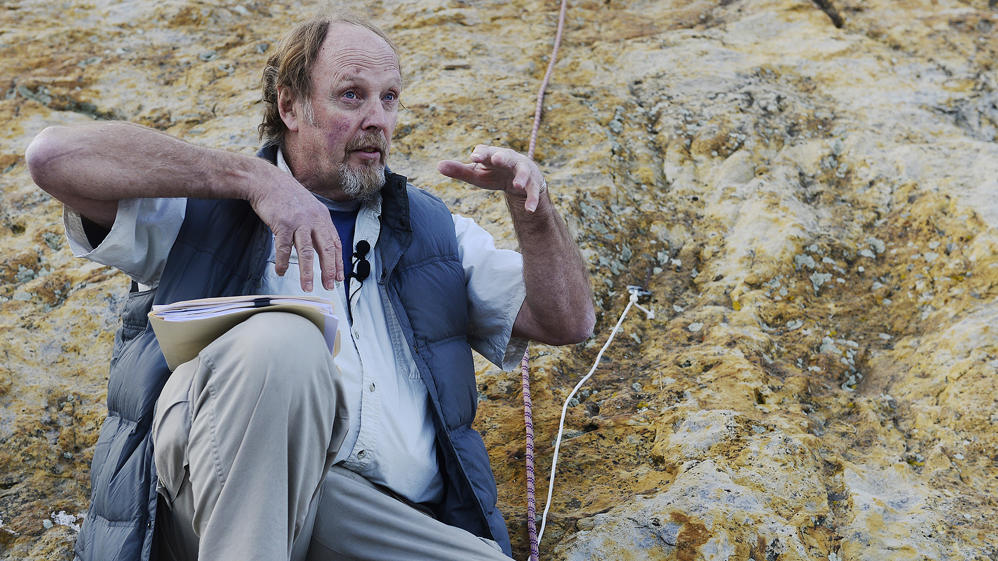 Paleontologist Martin Lockley sits in front of a rock with dinosaur claw marks and shows how dinosaurs must have clawed into the rock during a mating ceremony where they made pseudo nests for potential mates.