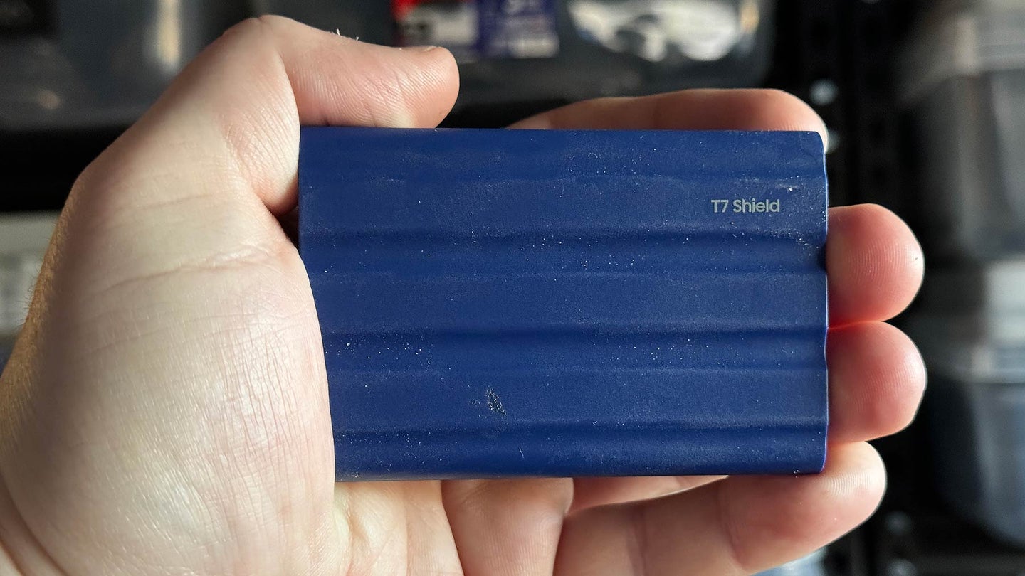 A hand holding a blue samsung T7 shield portable SSD