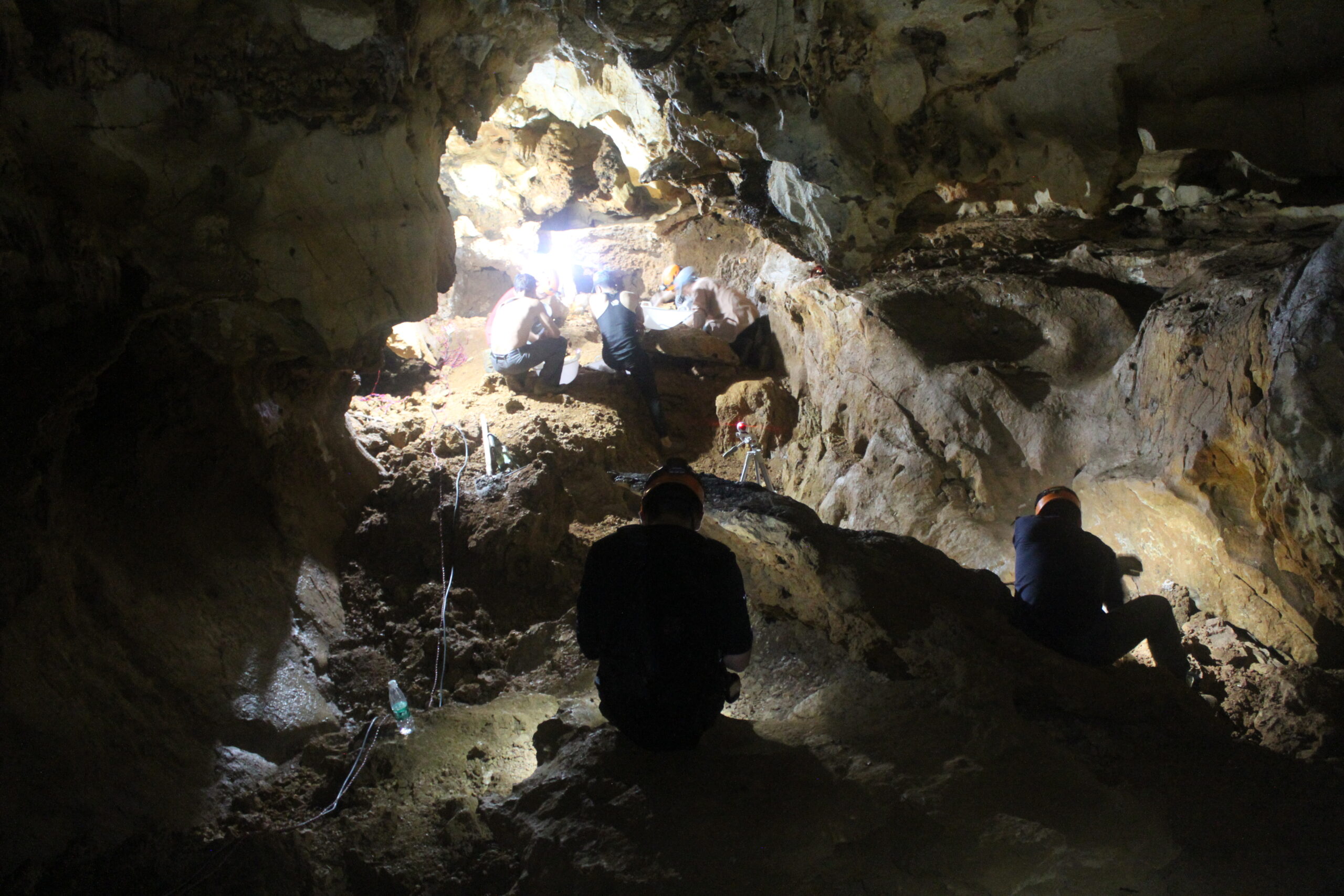 Two paleontologists are seen digging into hard cemented cave sediments.