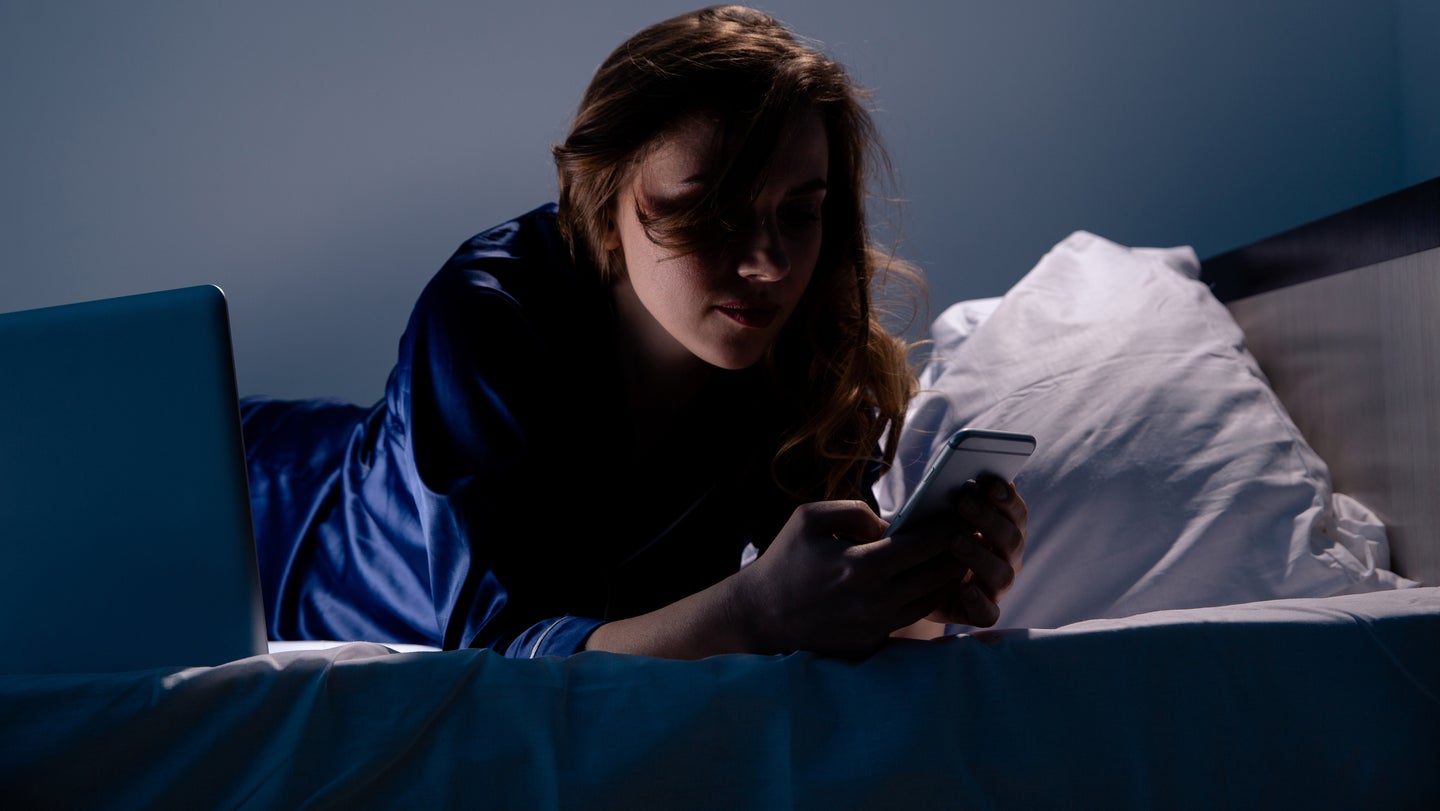 Woman on phone in bed in darkened room with face obscured