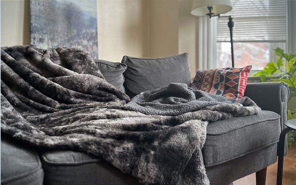A grey Chanasya Premium Wolf Faux Fur Throw Blanket on a blue couch.