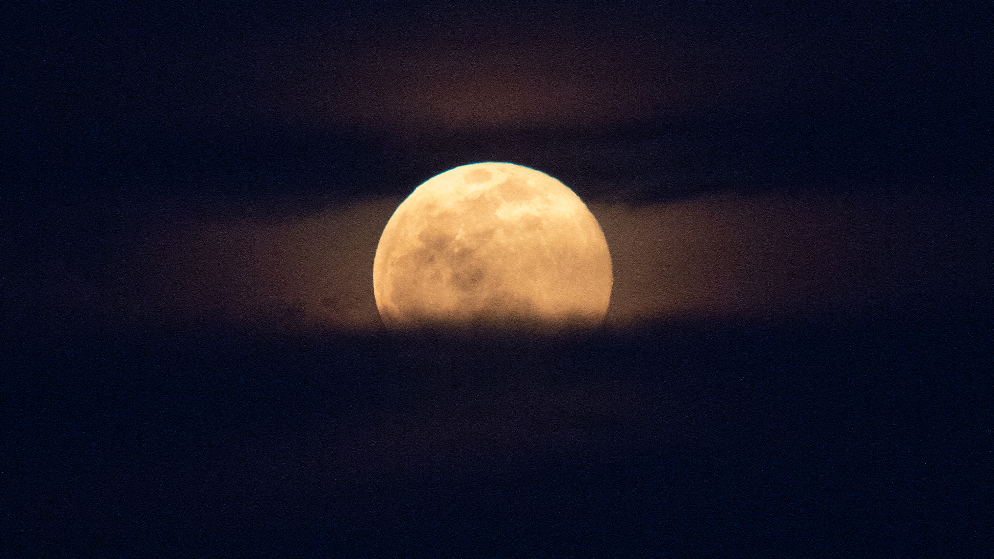 The full moon rises, with clouds below and behind it.