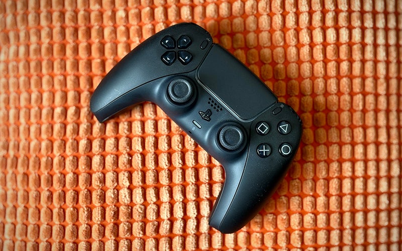 Black PS5 DualSense controller on an orange textured throw pillow