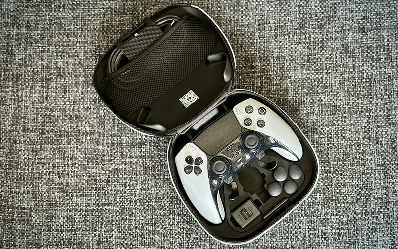 White and black PS5 DualSense Edge controller in its clamshell case on grey upholstery