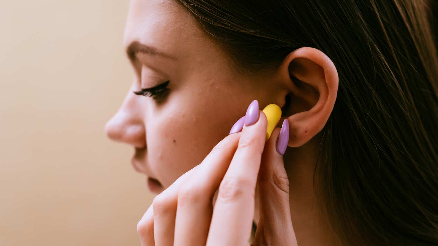 A woman puts a yellow earplug into her ear.