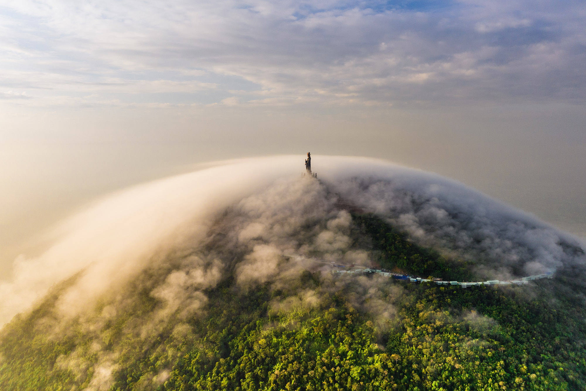 A Buddha statue at the top of a green mountain covered in a cloud