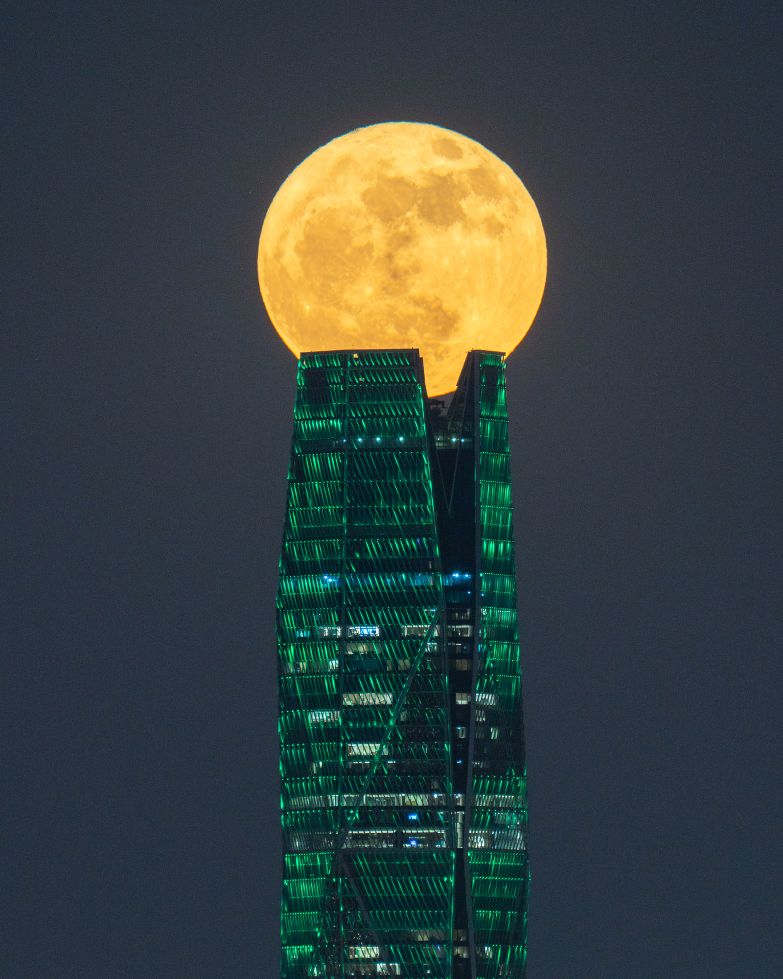 A full moon looks like it's resting on a tall building