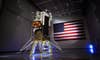 Intuitive Machinesâ Nova-C moon lander stands upright on six legs next to an American flag. 
