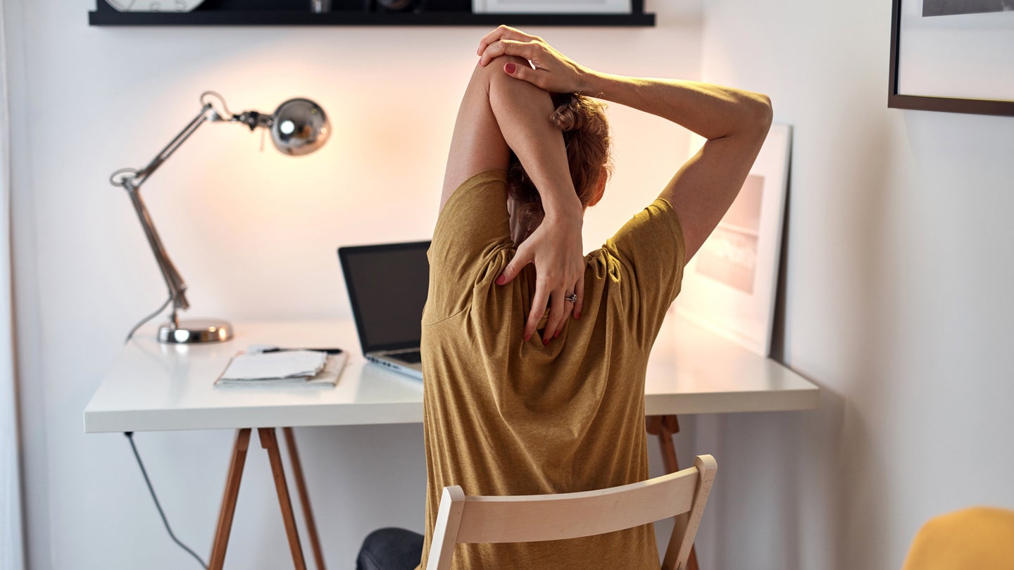 a person sitting at a computer stretches their arm behind their head