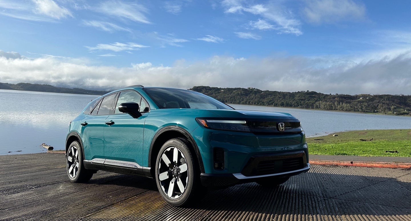 a greenish-blue SUV sits in front of a lake