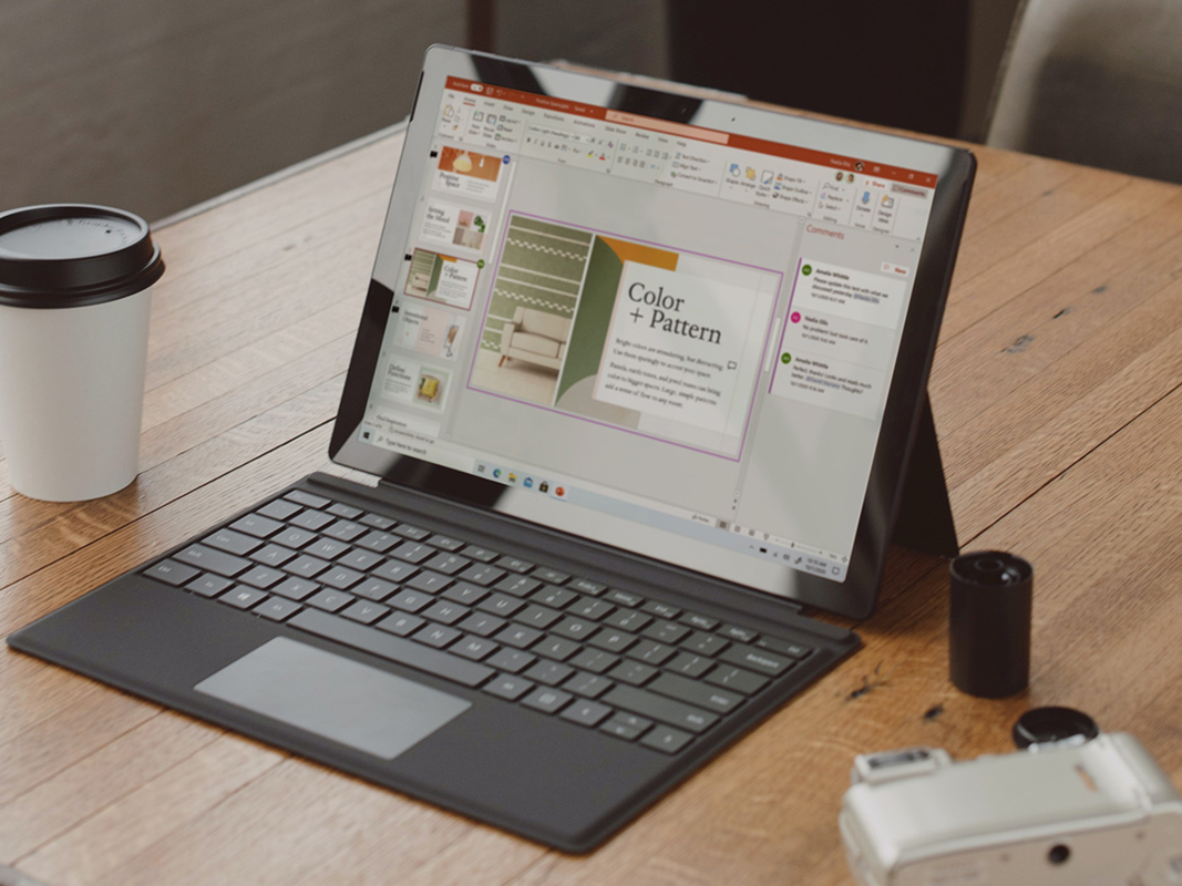 A Microsoft Surface laptop on a wooden desk with Microsoft Powerpoint open.
