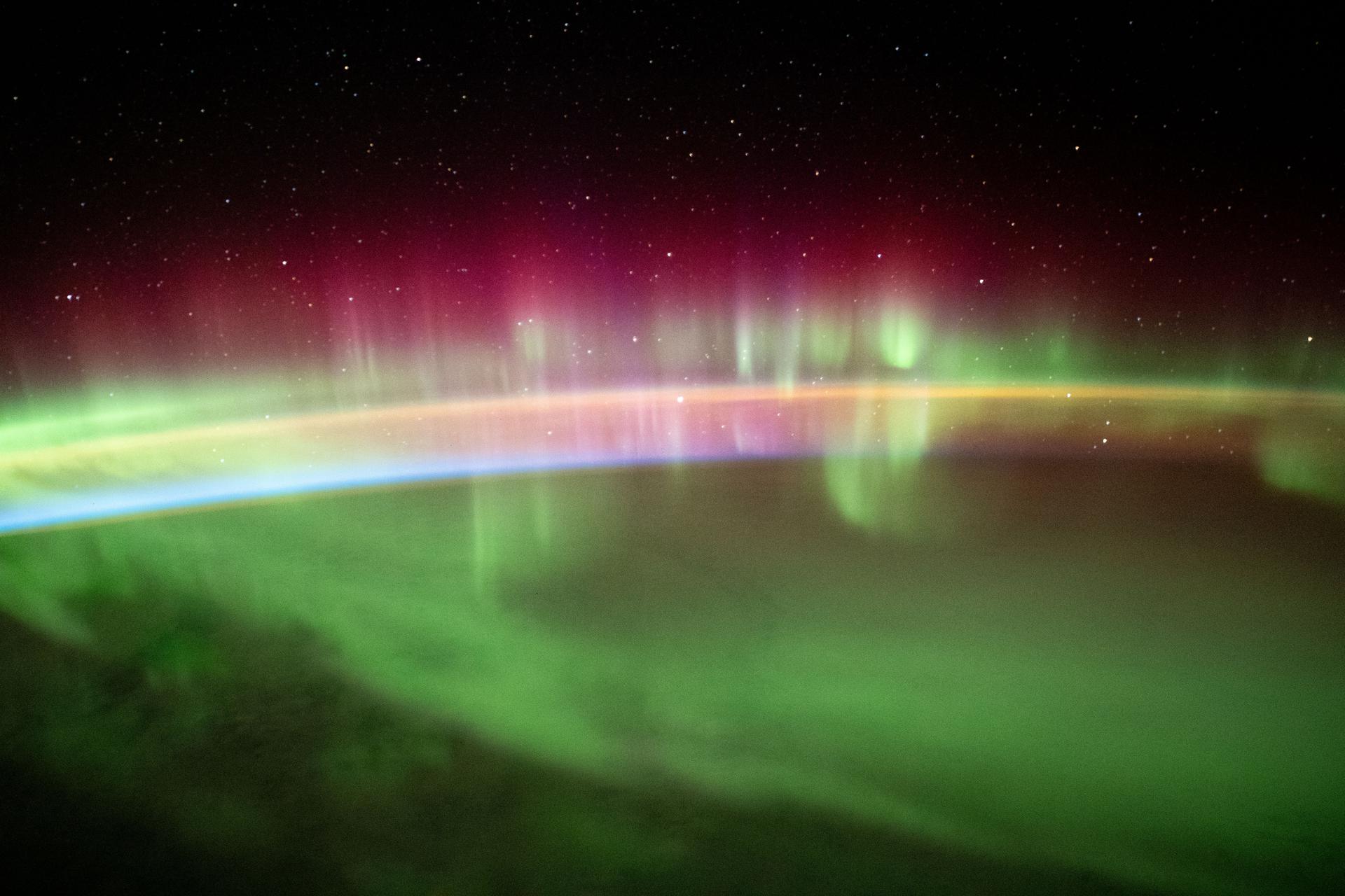 a green, yellow, purple, and blue aurora over the earth