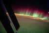 green and red aurora in the middle with a cloudy earth below and stars above