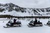 people riding snowmobiles in front of a hill and bison