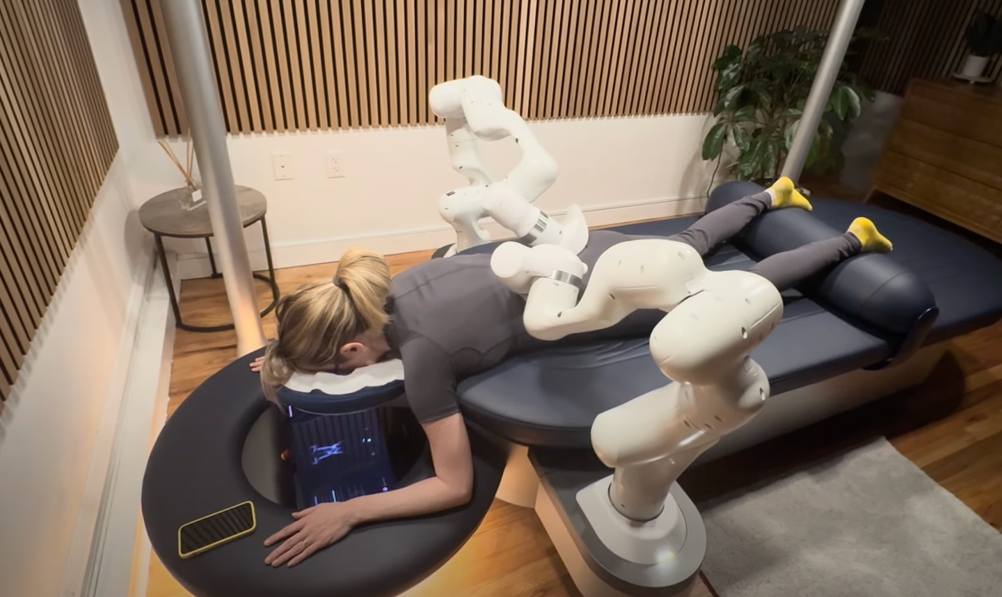 woman lays on blue table with two robot arms touching her back