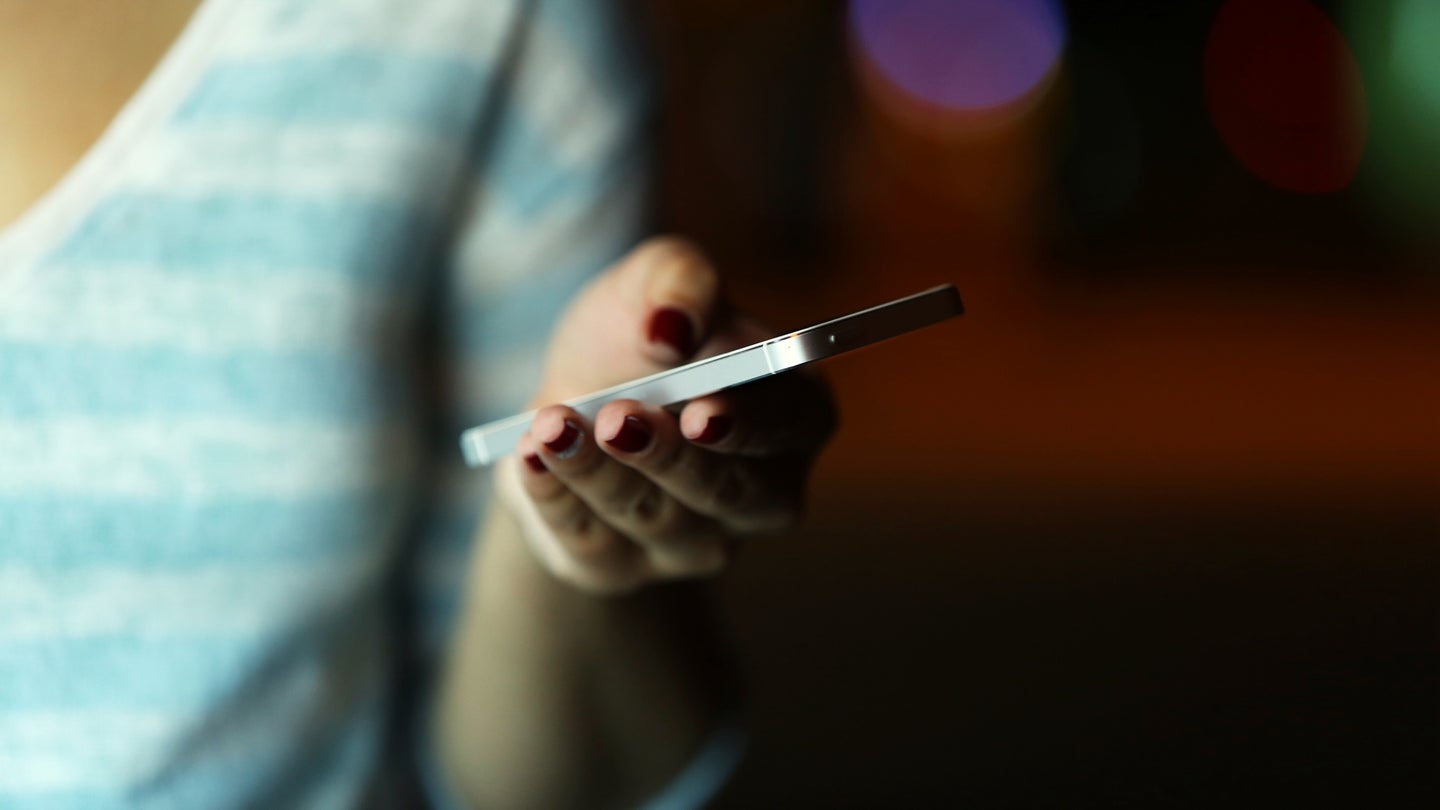 Female hand with mobile phone on blurred night lights background