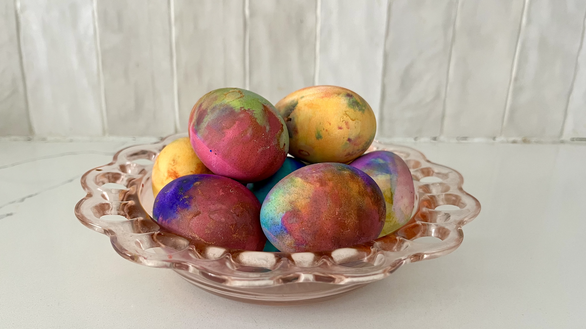 colorful eggs in a pink glass bowl on a white countertop