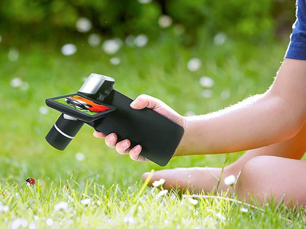 A person using a mini LCD microscope outdoors to look at grass.