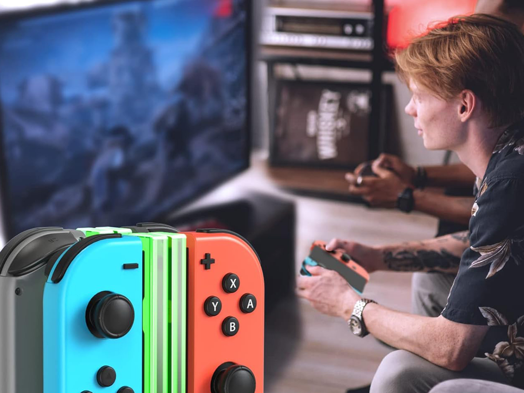 A person playing on a Nintendo Switch console and charging their Joy-Cons on a charging dock.