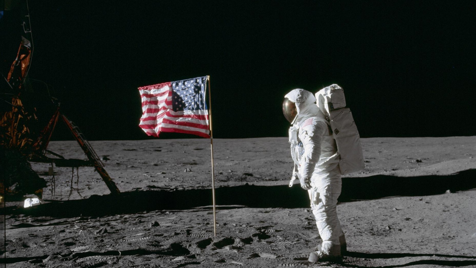 Buzz Aldrin on the moon next to American flag.