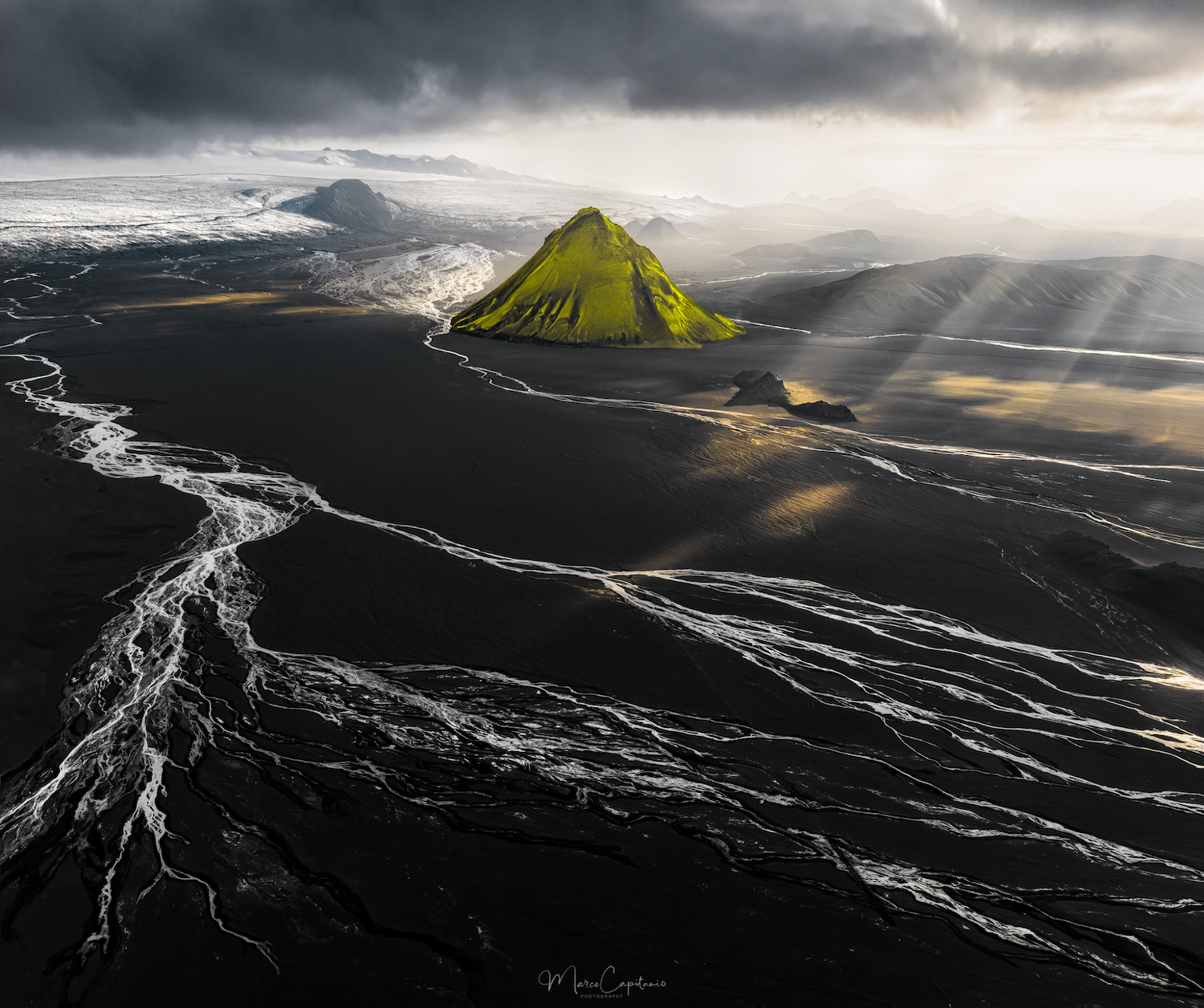 a green mountain stands by itself on black sand
