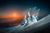 sharp, snow-covered rocks jut out the side of a mountain as four drone lights shine down. the sun sets in the background