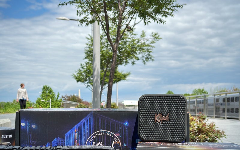 Black Square Klipsch Austin best portable Bluetooth speaker on top of boxes with the Washington Monument and VRE train in the background