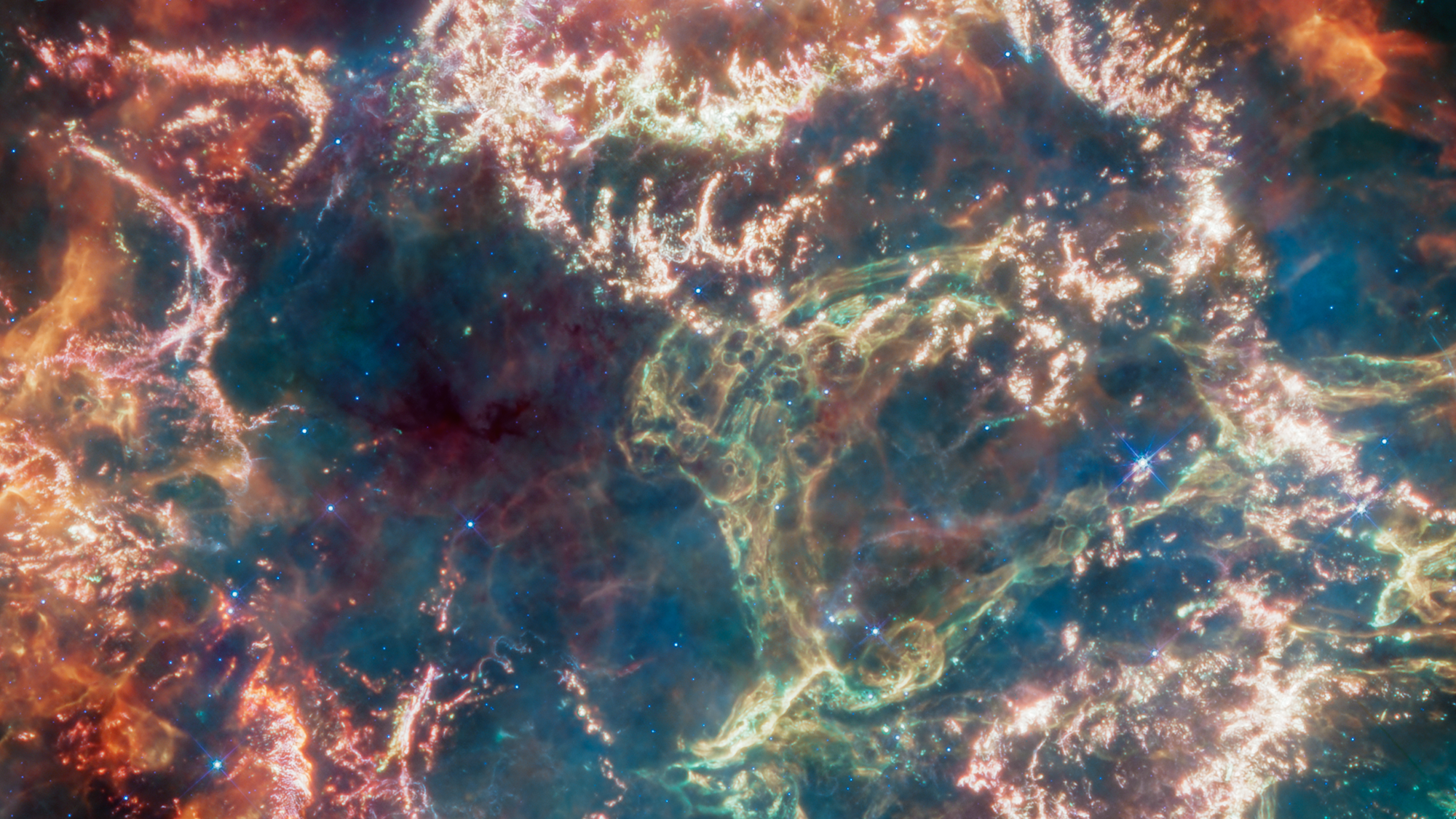 Cassiopeia A (Cas A) is a supernova remnant located about 11,000 light-years from Earth in the constellation Cassiopeia. It spans approximately 10 light-years. This image uses data from Webb’s Mid-Infrared Instrument (MIRI) to reveal Cas A in a new light. This image combines various filters with the color red assigned to 25.5 microns (F2550W), orange-red to 21 microns (F2100W), orange to 18 microns (F1800W), yellow to 12.8 microns (F1280W), green to 11.3 microns (F1130W), cyan to 10 microns (F1000W), light blue to 7.7 microns (F770W), and blue to 5.6 microns (F560W).