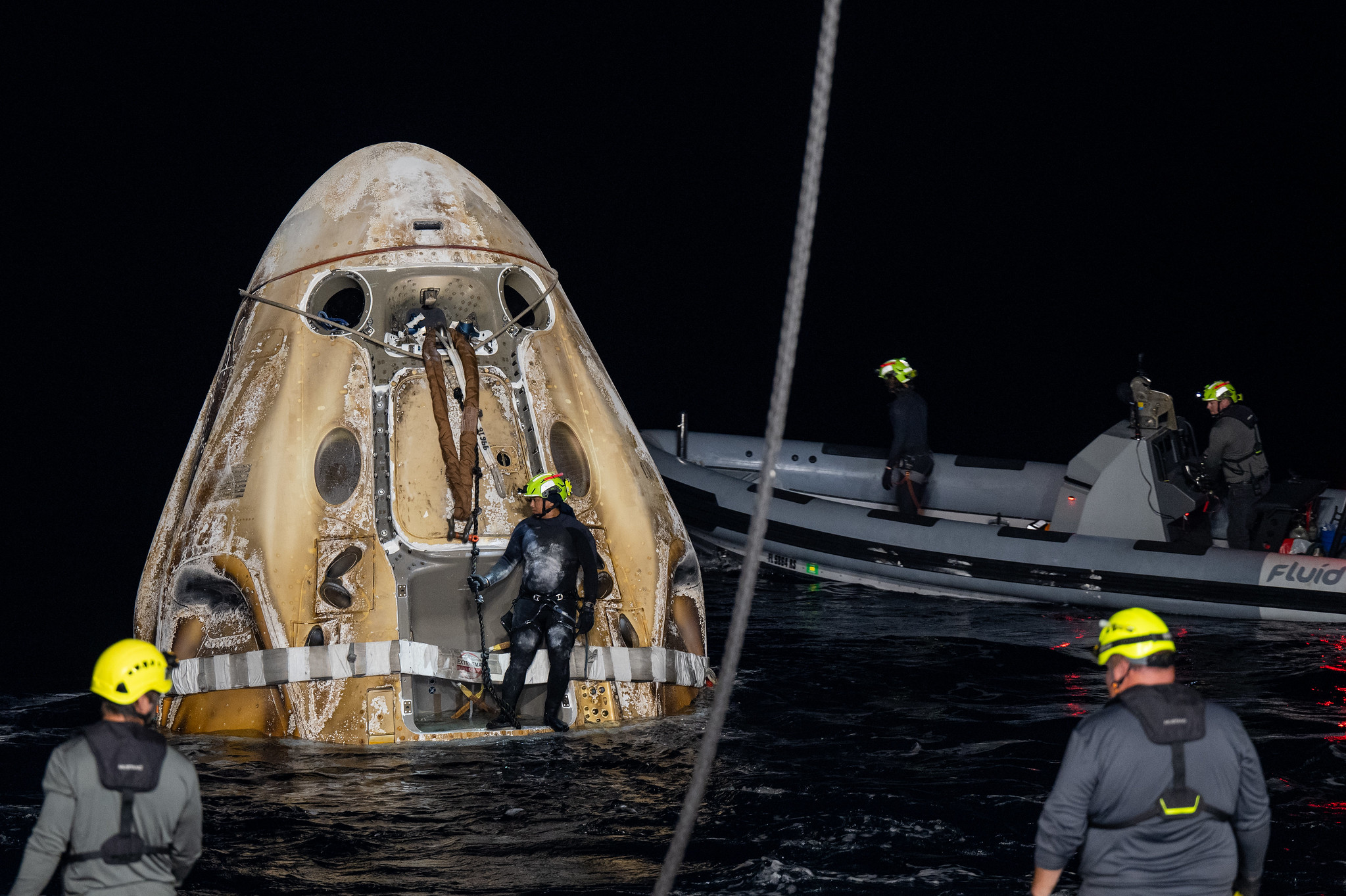 a spacecraft floats in the water as people in helmet look from boats