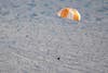 a white and orange parachute with a capsule attached flies down from the sky into a sandy landscape