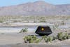 a black capsule sits on desert sand near shrub brush