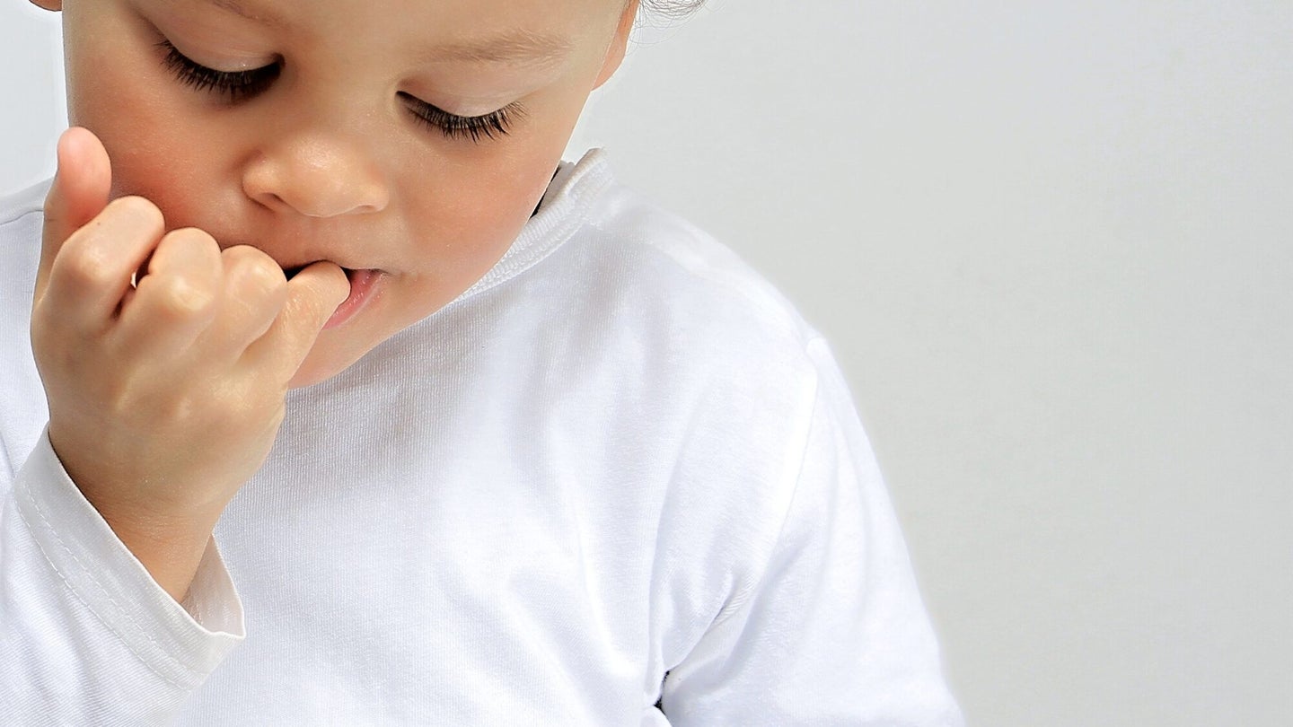 Little boy biting his nails on grey background