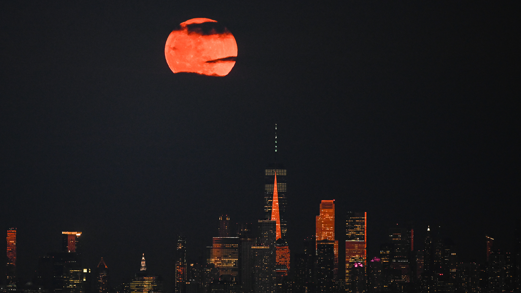 a pink-hued full moon rises above the new york city skyline