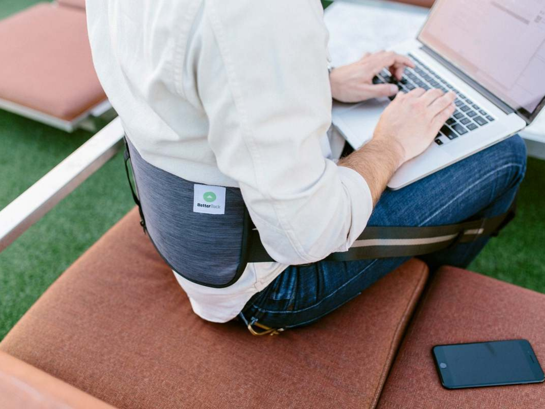 A person typing at a laptop wearing a back support brace.
