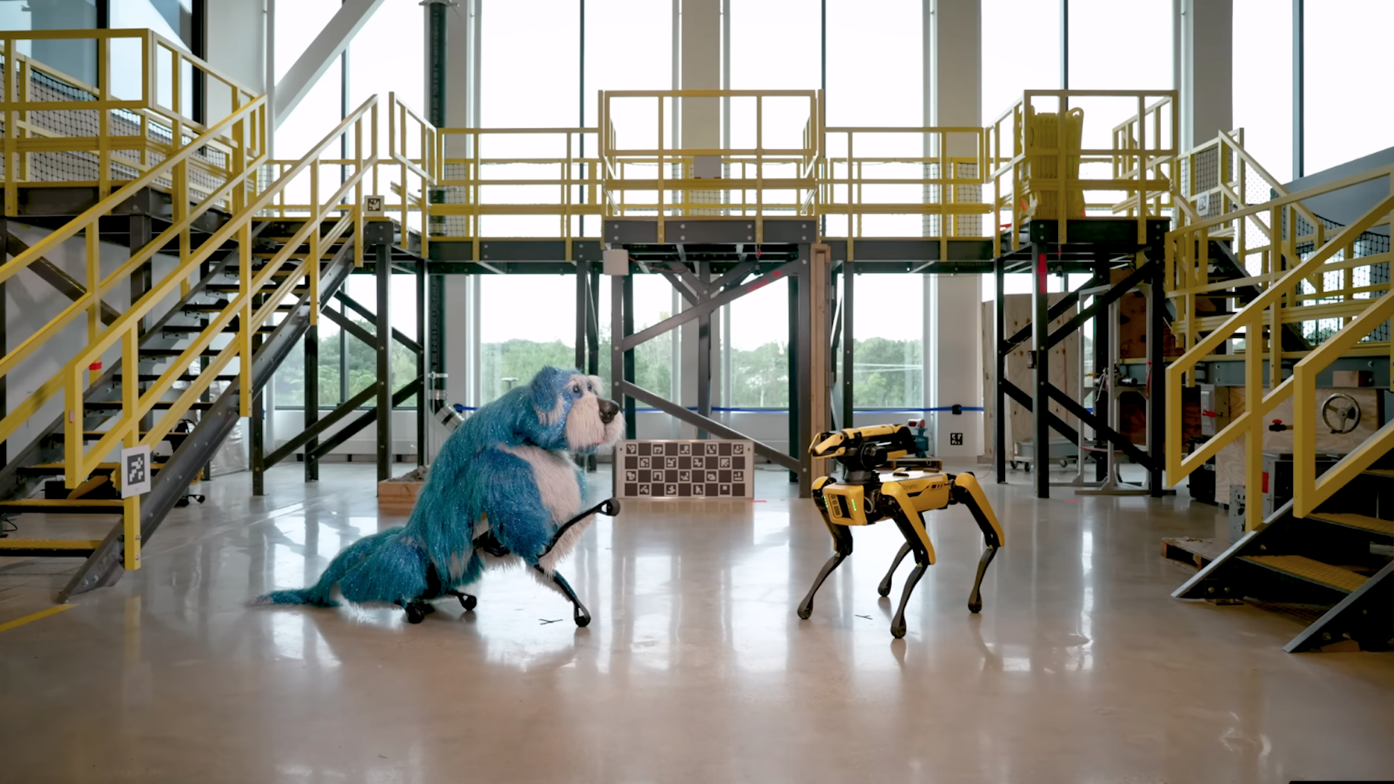 Boston Dynamics Spot robot in puppet dog costume sitting next to regular Spot robot.