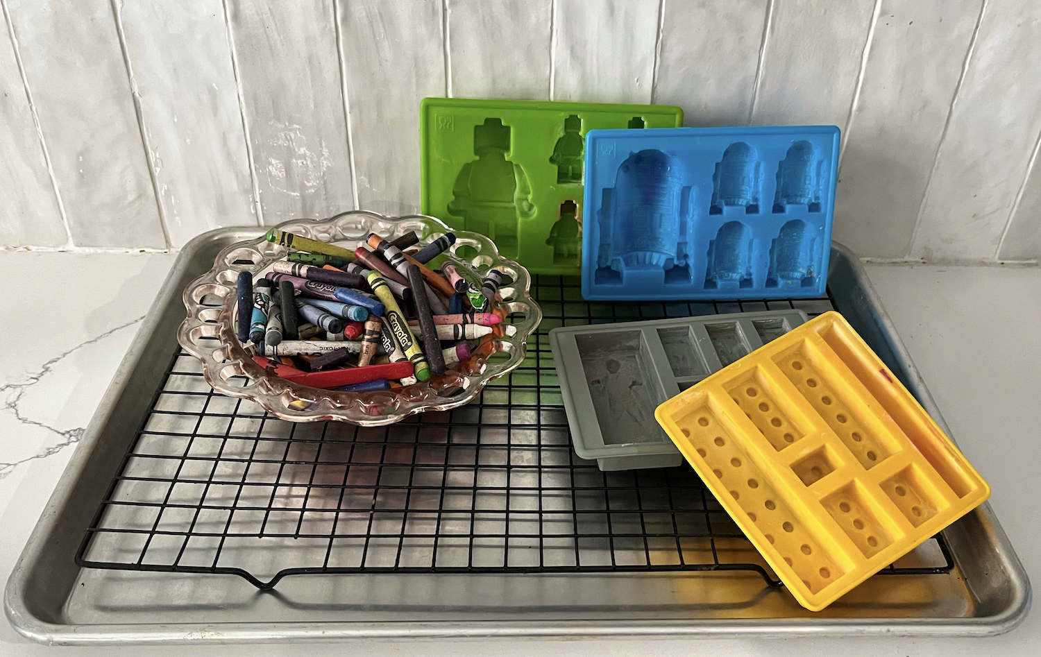 crayon melting supplies on a kitchen countertop: crayons, molds, baking sheet, wire rack