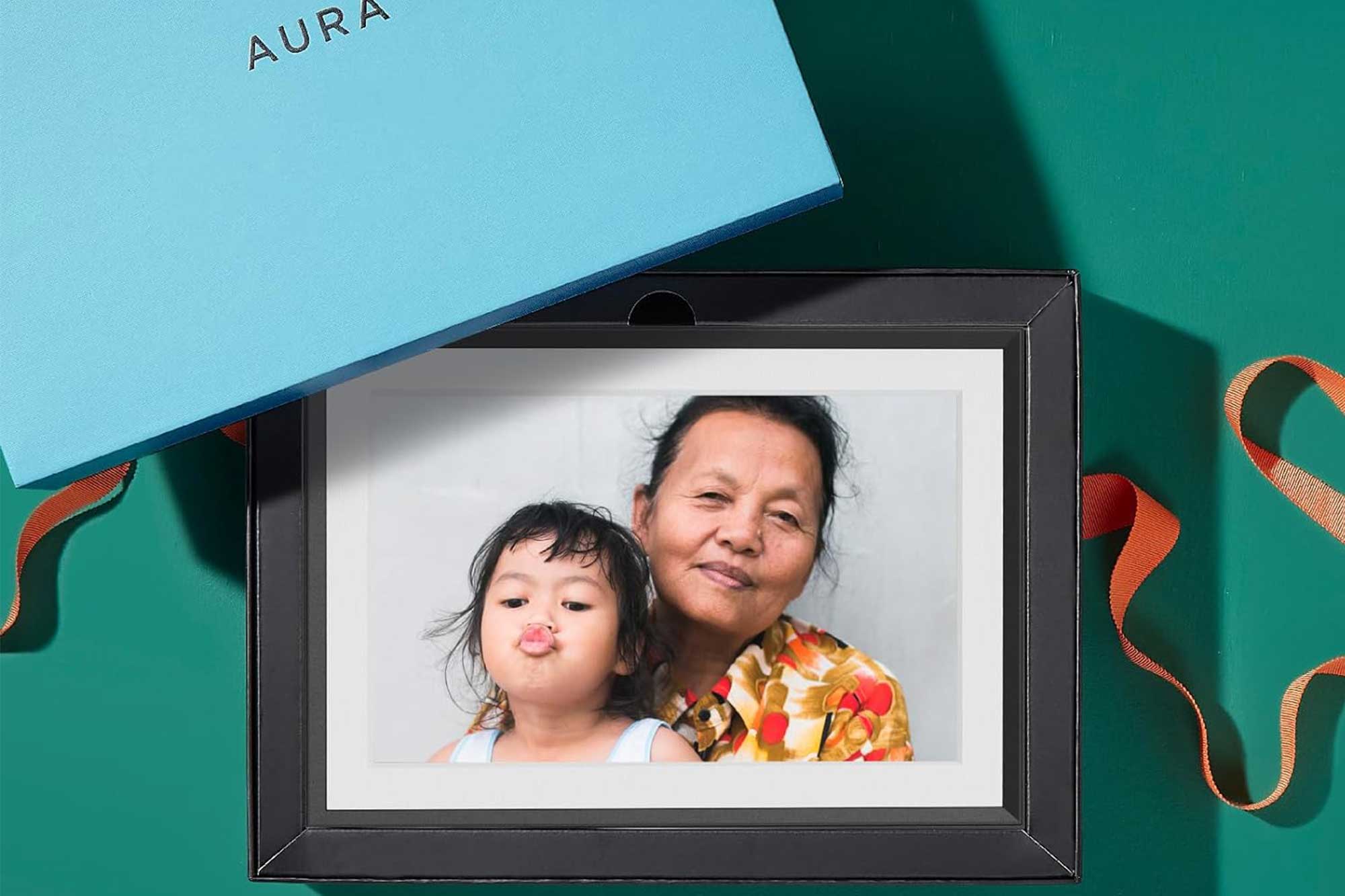 An Aura picture frame near a gift box with a grandma and child displayed on it.